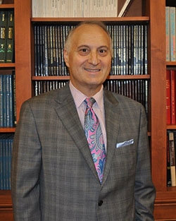 Dr. Samuel Beran smiles at the camera while standing in front of a bookcase.